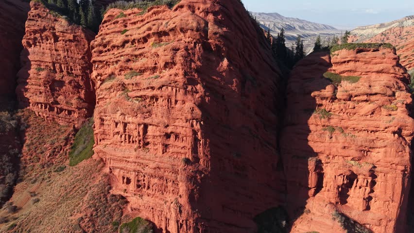 Cinematic pull-out shot revealing the majestic red sandstone cliffs and jagged peaks of Jeti-Oguz in Kyrgyzstan under bright midday sun.
