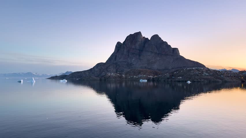Landscape of Greenland with mountains, icebergs, and calm water in the evening light near the fjord