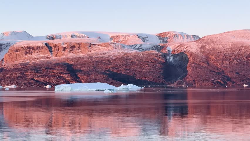 Landscape of Greenland with mountains, icebergs, and calm water in the evening light near the fjord