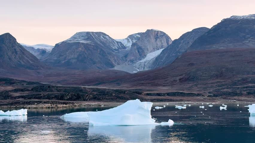 Landscape of Greenland with mountains, icebergs, and calm water in the evening light near the fjord