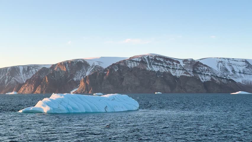 Landscape of Greenland with mountains, icebergs, and calm water in the evening light near the fjord