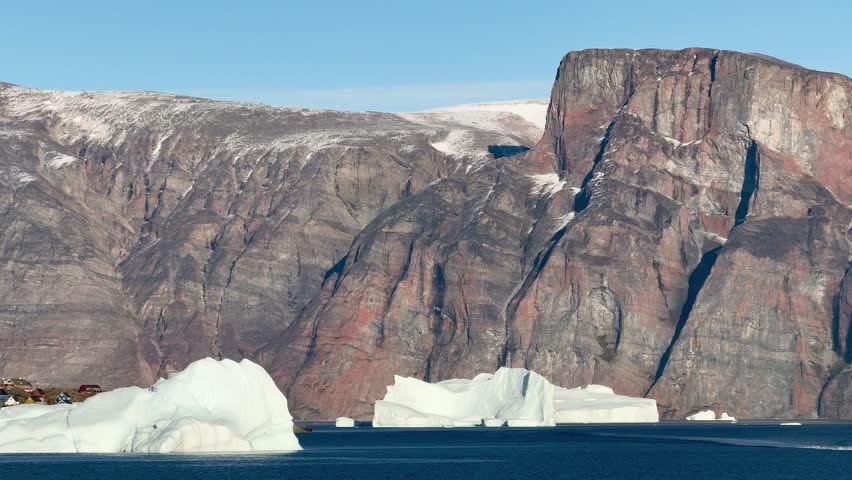 Landscape of Greenland with mountains, icebergs, and calm water in the evening light near the fjord