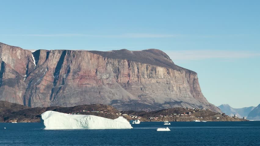 Landscape of Greenland with mountains, icebergs, and calm water in the evening light near the fjord
