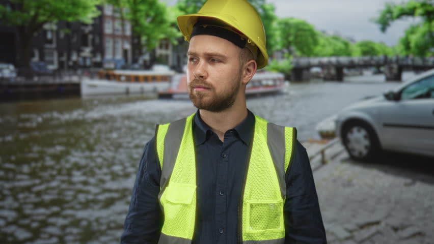 Man in yellow hardhat and high visibility vest pointing finger on a street in amsterdam; construction safety confidence.