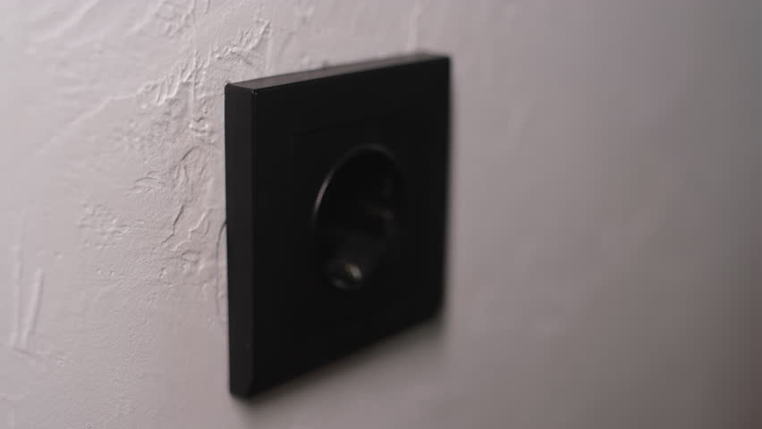 Hand plugging phone charger into power socket