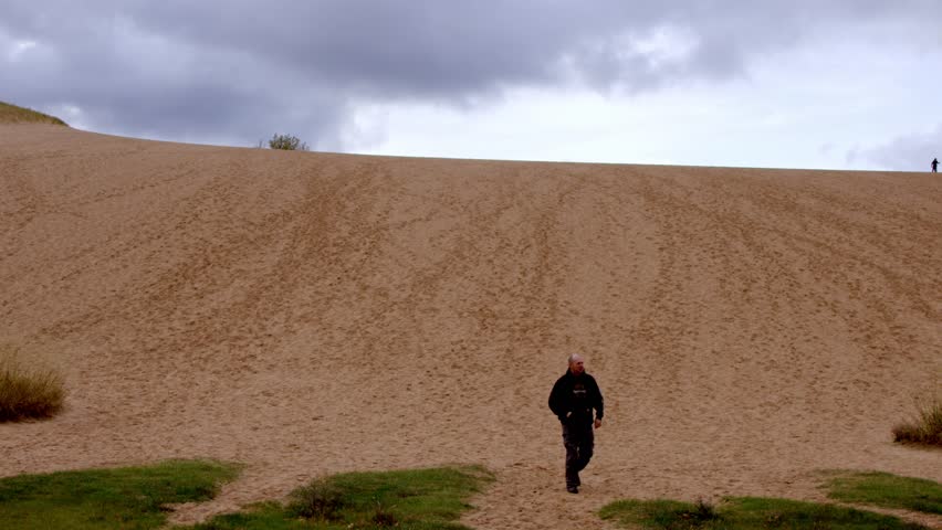 Middle aged man walking down Dune Climb at the Sleeping Bear Dunes National Lakeshore in Michigan with stable video shot.