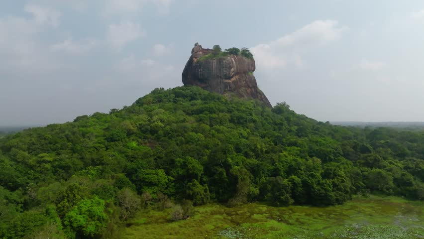 Sri Lanka drone approach toward Sigiriya Rock Fortress over dense jungle canopy and lush greenery.