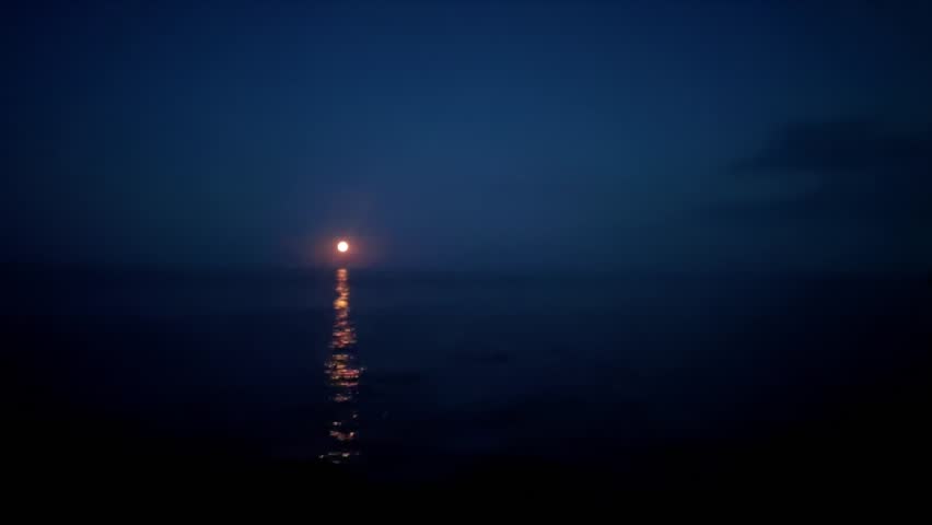 Full moon rising over calm sea at night with moonlight reflection on water surface. Dark blue sky and peaceful atmosphere. Meditation and relaxation content