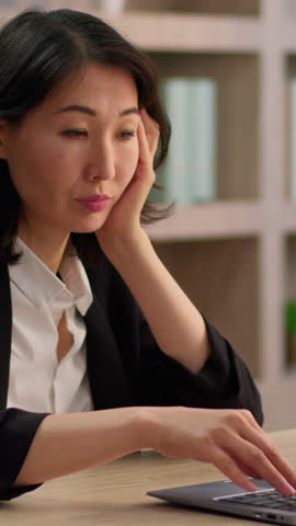 Asian adult businesswoman feeling sad fatigue sleepy working laptop middle-aged business woman work computer boring using technology corporate software Chinese female Korean lady weak upset in office