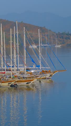 Vertical video: passenger boat sailing through the marina with multiple yachts and gulets moored along the harbor in Fethiye, Turkey. Passenger boat moving through calm waters