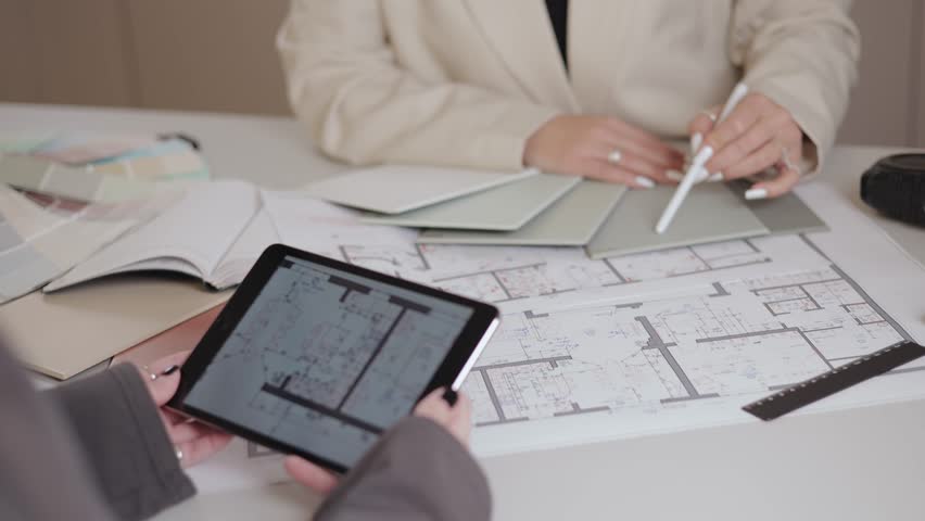 Female architects interior designer reviewing building blueprints and color swatches for project planning with client.