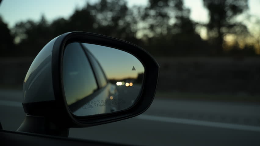 Blur reflection in the side mirror of driving car on the road on evening time. View from front passenger seat. 
