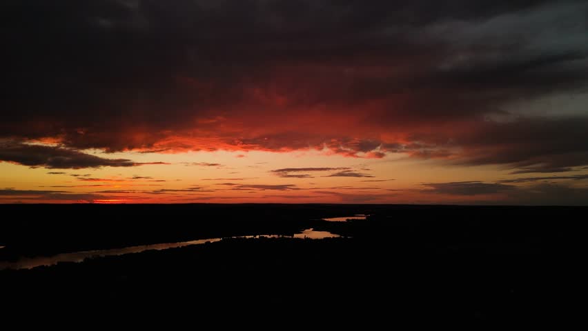 Fast aerial sunset panorama over river under dramatic clouds. Dynamic drone pan over river at sunset, dark clouds and glowing horizon, cinematic natural background.