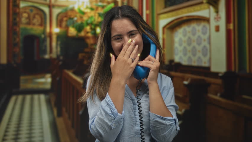 Woman holding blue telephone handset and covering mouth while smiling in church building; joy gratitude.