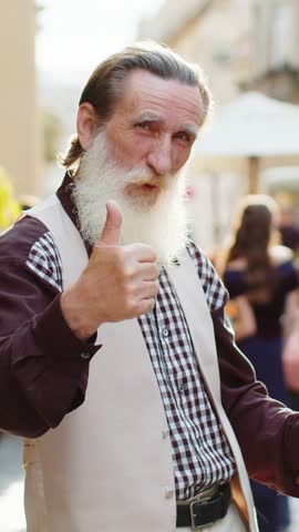 Like. Happy bearded senior old man looking approvingly at camera showing thumbs up sign positive something good positive feedback. Elderly mature grandfather standing in urban city sunshine street