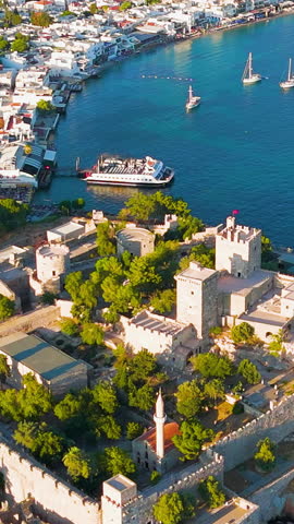 Vertical video. Bodrum, Turkey. Evening aerial drone view of Bodrum Castle illuminated by sunset, with yachts in bay, beaches and white houses on coastline. Aerial View, MasterShots, Dronie. Rich colors