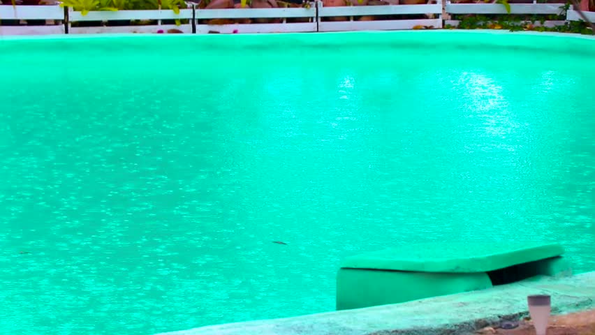 Rainy tropical resort hotel with palm trees jungle pool turquoise blue water and monsoon rain drops drips dripping in Mai Khao on Thalang District Phuket Province island in Thailand.