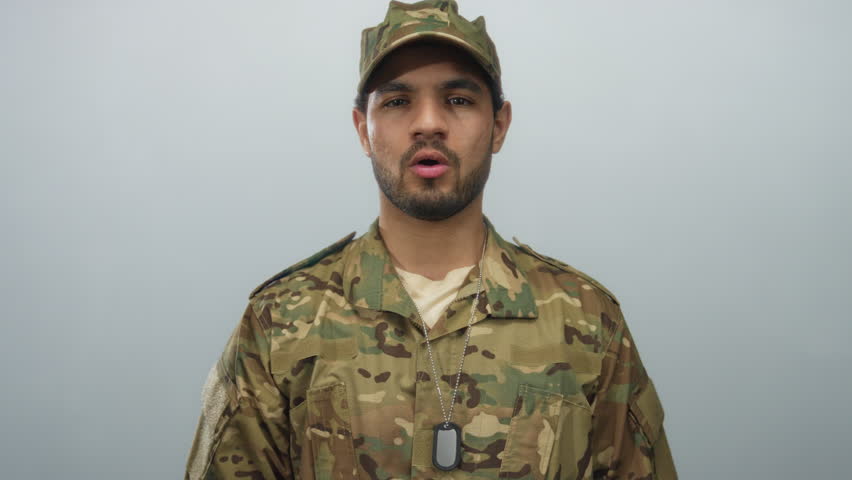 Man in camouflage uniform with dogtags speaks in studio against gray background; pride duty courage honor.