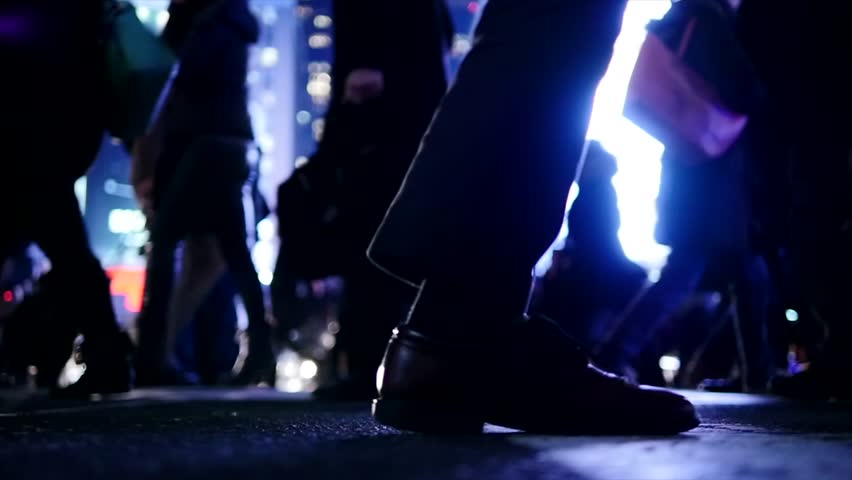 People crossing a city street at night under urban lights, showing everyday life, pedestrian movement, nightlife, and modern city living.