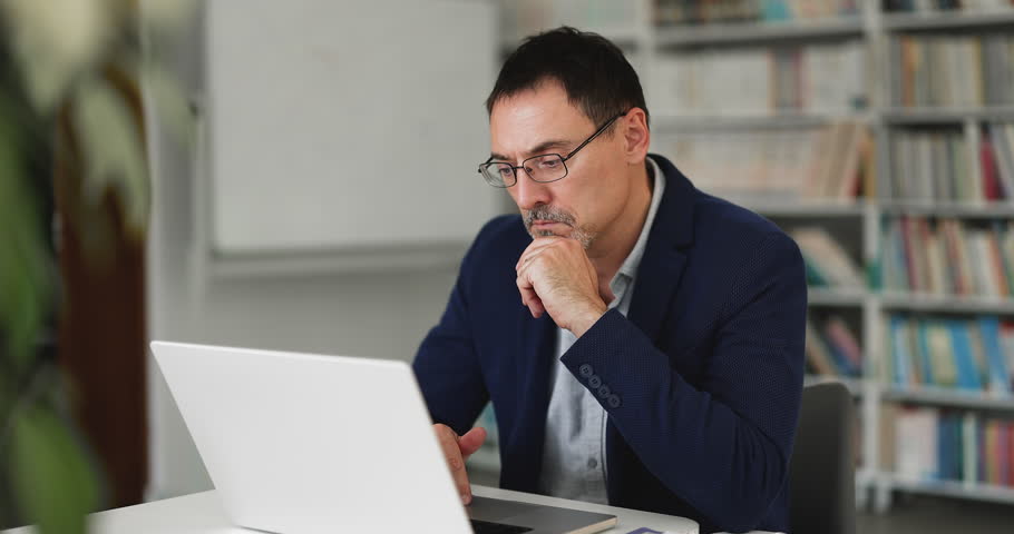 Focused middle-aged 50s business man working online using laptop, search issue solution, making business decision, solving problem, thinking on task or researching, reviewing information in office