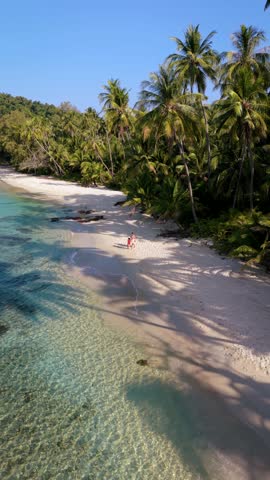 Bask in the serene environment of Koh Kood, Thailand, where soft sands meet crystal-clear waters. A couple of men and women walk on the beach, relaxing at this tropical paradise.