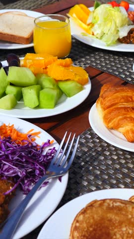Morning sunlight illuminating a delicious and colorful breakfast buffet on a wooden table, with a person picking up a piece of fresh cantaloupe melon with a fork for a healthy start to the day