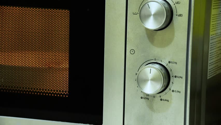 A hand removes a plate of hot food from the microwave. Side view at an angle. Close-up.