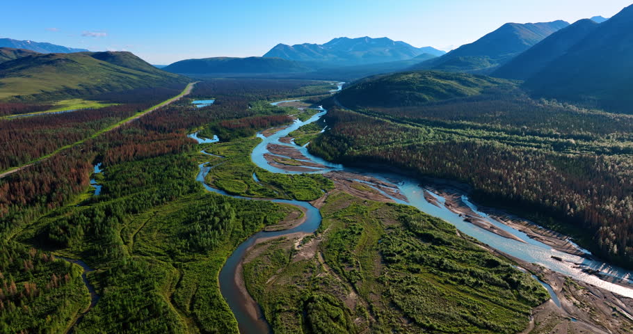 Flight over the spectacular wilderness of Alaska. River flowing among the woods and mighty mountains.