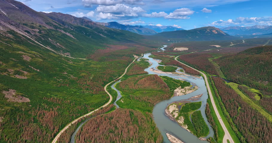 Flying above the delta of the river near the highway. Stunning mountains range in Alaska.
