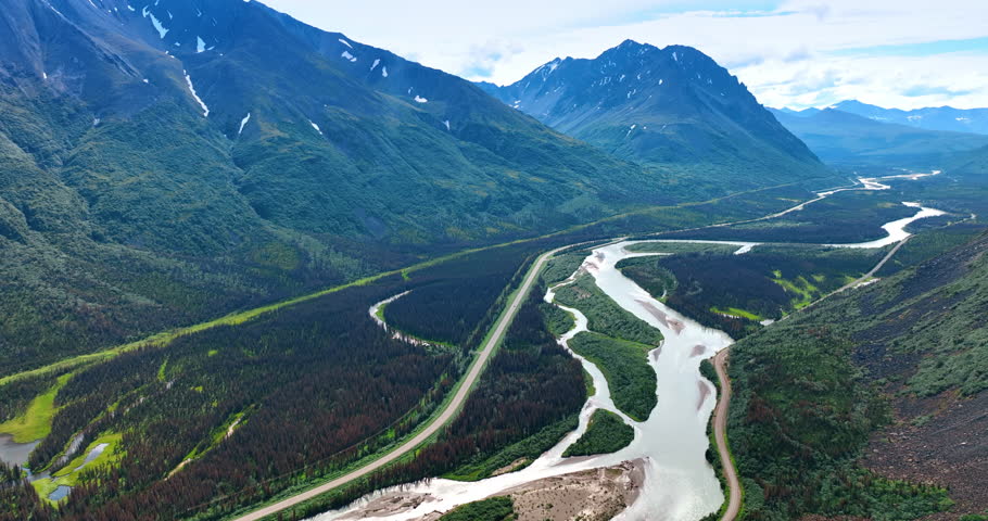 Huge verdant mountains surround the delta of the branching river. Breath-taking wilderness of Alaska. Aerial view.