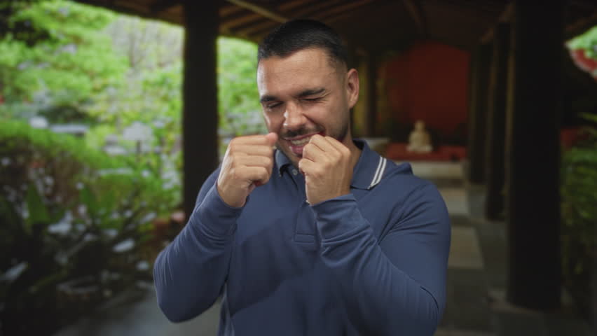 Young hispanic man raises fist in boxing pose at hotel lobby; confidence determination discipline focus.