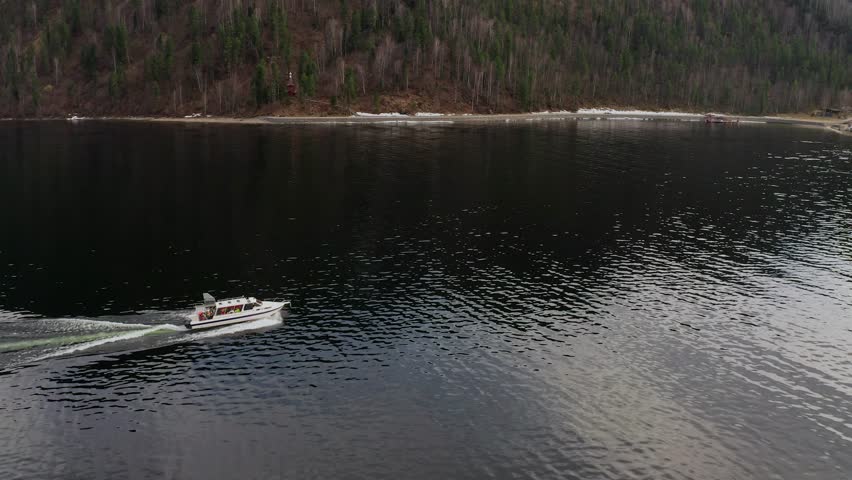 Shooting from a drone flying over a mountain lake, along which a speedboat is moving. A motorboat is rushing towards the hotel on the shore.