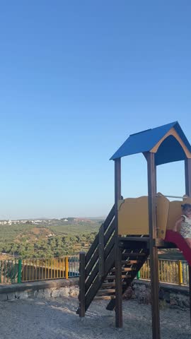 Vertical cute footage: little girl sliding down on playground, happy child playing outdoors, kids activities, fun childhood time