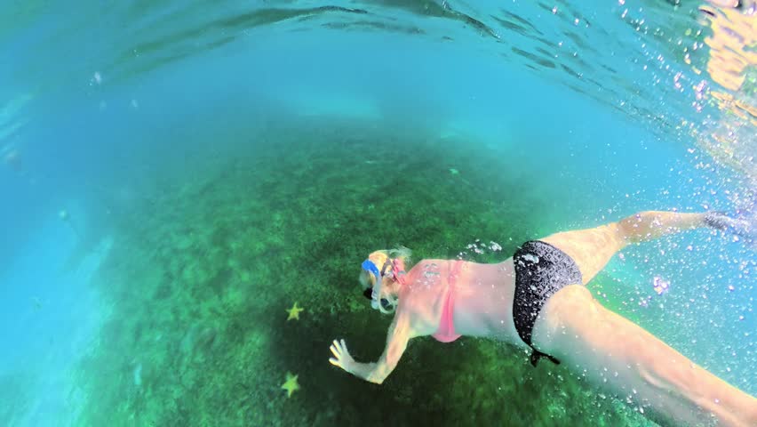 Woman snorkeling with starfishes in Plage de Grande Anse d'Arlet, Martinique, Carribean of France