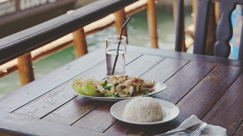 Thai food in an authentic rustic restaurant near the sea. Tradition fried Pad Thai noodles and boiled rice close up on the table, impressions and tastes on solo trip through the province of Thailand