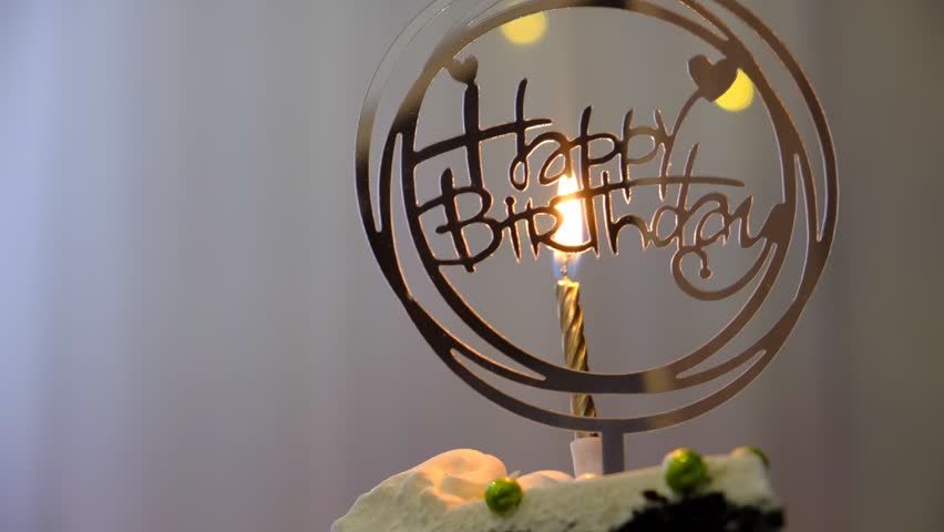 Happy Birthday text, candle burning. Birthday cake with white cream cheese, cake tier. Delicate lambeth style birthday cake with white cream cheese, festive background with string lights.