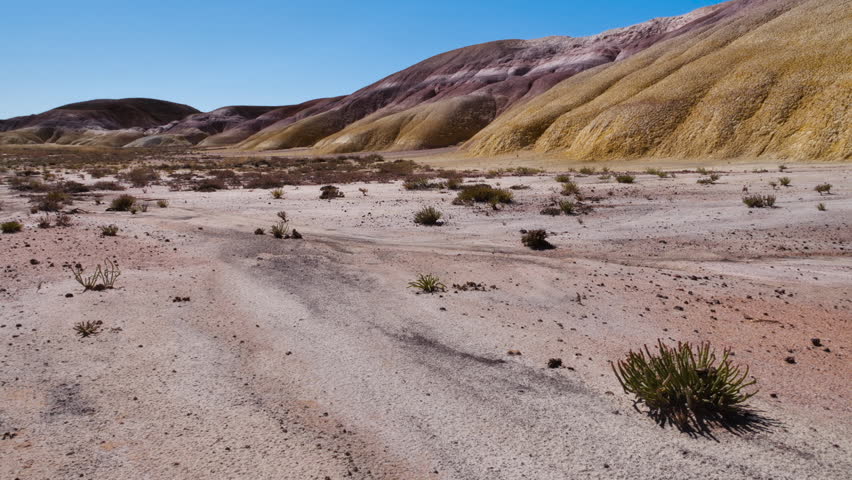 A desert, arid area subject to erosion against a backdrop of colorful hills.