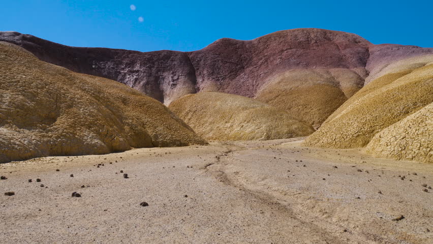A desert, arid area subject to erosion against a backdrop of colorful hills.