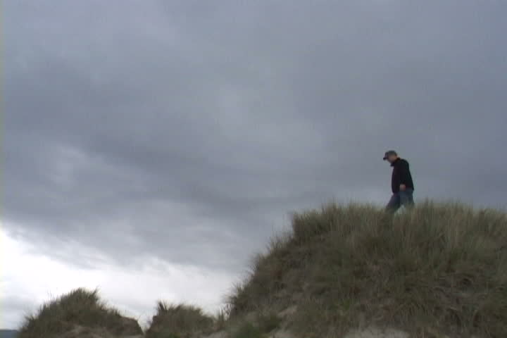 Man on sand dune in Oregon searches from high point.