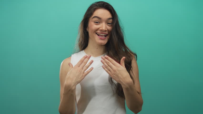 Young hispanic woman smiling places hands on chest showing bare shoulders in studio with teal wall; gratitude sincerity.