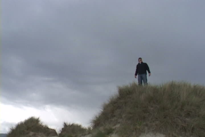 Man reaches for the sky atop sand dune in Oregon.