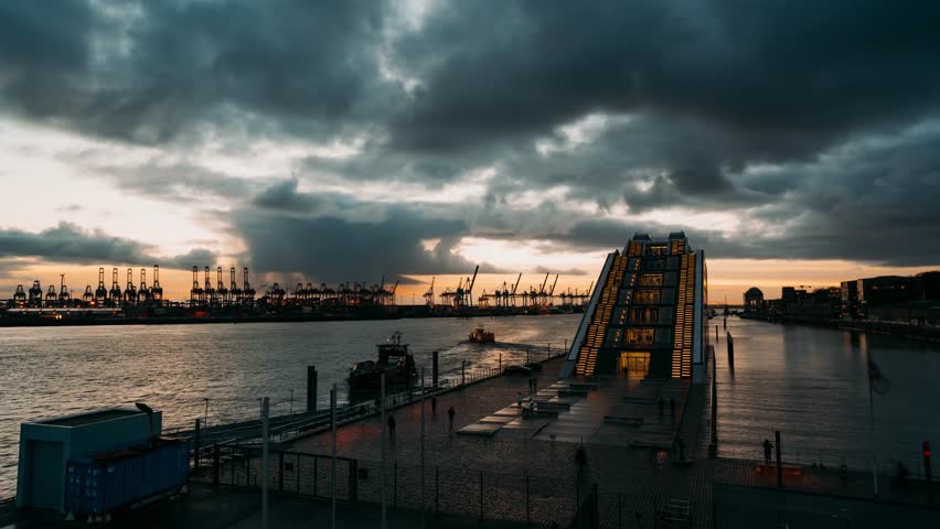 HAMBURG, GERMANY – Day to night timelapse of the Dockland office building. Modern glass architecture on the Elbe River with port cranes and dramatic clouds at sunset.