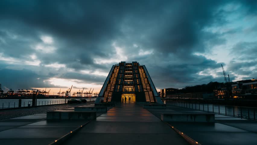HAMBURG, GERMANY – Day to night hyperlapse of the Dockland office building. Modern glass architecture on the Elbe River harbor during a dramatic sunset transition.