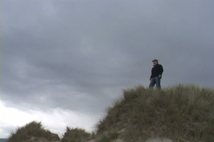 Man on sand dune in Oregon puts arms up in accomplishment