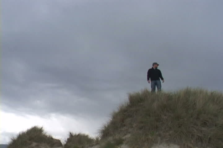 Man on sand dune in Oregon points out in a direction.