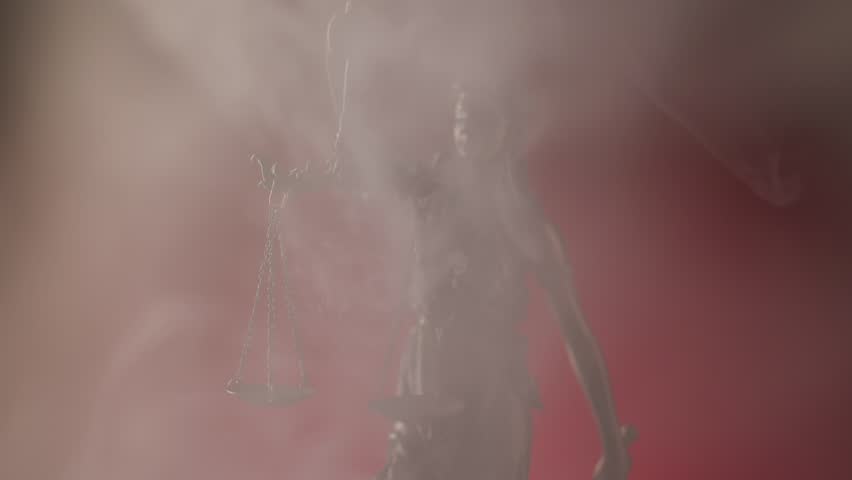 Bronze Lady Justice statue holding scales and sword signifying impartiality surrounded by swirling smoke on red background.