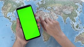 Smartphone with green screen held over a world map as a hand points to a location - Powered by Shutterstock - Get 15% off with code: PIKWIZARD15