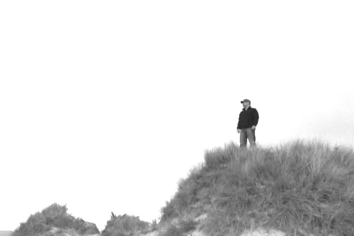 Man on sand dune in Oregon points out in a direction, black and white film