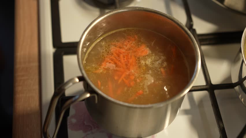 The soup is cooked on the stove and stirred with a large spoon