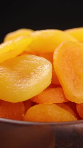 Pile of dried apricots fruit in brown wooden bowl rotating slowly on balck background, Close-up view
